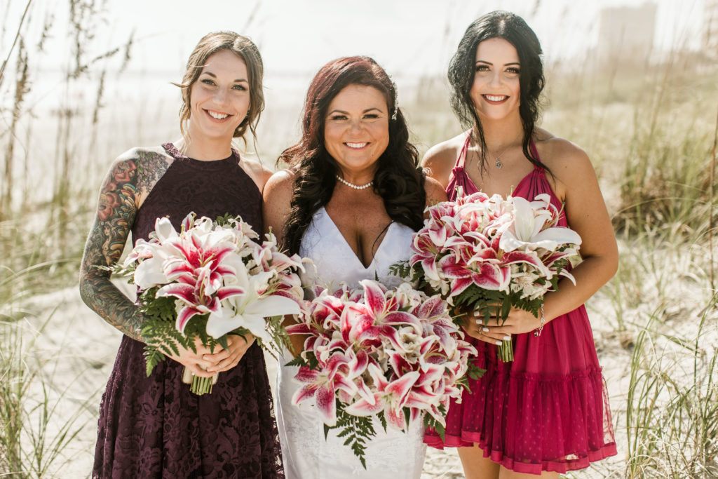 3 women on a beach in bright colored dresses for a beach wedding
